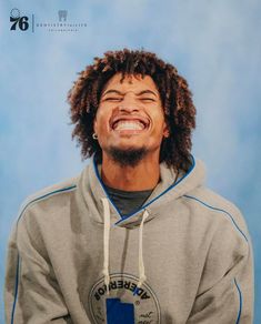 a man with dreadlocks is smiling and wearing a grey hoodie that has blue trim