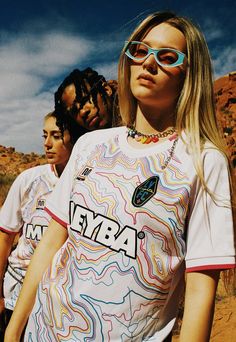 two women wearing sunglasses standing next to each other in front of some rocks and dirt