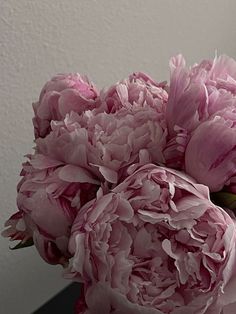 a bouquet of pink peonies sitting in a vase on a counter top next to a white wall