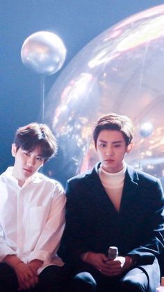 two young men sitting next to each other in front of a mirror ball with bubbles