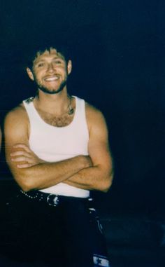 a man with his arms crossed standing in front of a black background and smiling at the camera