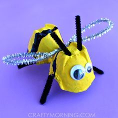 a yellow and black paper mache insect with eyes on it's head, sitting in front of a purple background