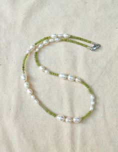 a green beaded necklace with white pearls and a silver clasp on a beige cloth