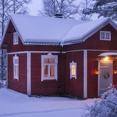 a red house is covered in snow and lit up with christmas lights on the windows