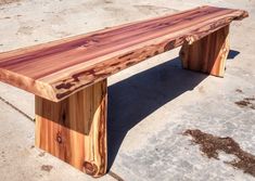 a wooden bench sitting on top of a cement floor next to a parking lot with no one around it