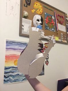 a person holding up a paper cut out of the shape of a bear in front of a wall with pictures on it