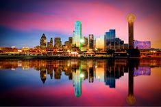 the city skyline is lit up at night with its lights reflecting in the still water