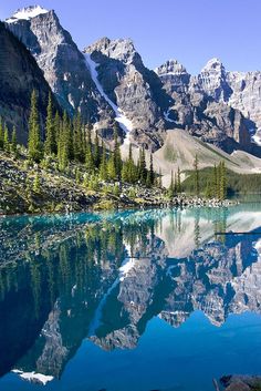 a mountain lake surrounded by pine trees and snow covered mountains in the distance with blue water