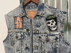 Let your rebellious side out in this vintage 1990's denim vest. A classic trucker vest in awesome stonewash denim. It features a turn down collar, metal buttons, two front patch pockets with flaps and two hand-warmer pockets.  It has been hand decorated with Iron Maiden and Misfits patches on the front plus a large Jack Daniels patch on the back. It also has a silver skull stud on the collar.  One of a kind Size Small. Measurements:                                                                                                                    Chest: 92 cms / 36 inches                                                                                                Length: 61 cms / 24 inches        BUYING VINTAGE: While all care is taken to state any obvious faults, please note that when yo Cotton Grunge Denim Vest For Streetwear, Grunge Cotton Denim Vest With Pockets, Light Wash Cotton Denim Vest For Streetwear, Fitted Punk Cotton Denim Jacket, Fitted Punk Style Cotton Denim Jacket, Fitted Cotton Punk Denim Jacket, Fitted Washed Denim Jacket In Grunge Style, Fitted Denim Vest Grunge Style, Fitted Grunge Denim Vest