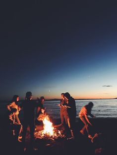 group of people standing around a campfire at the beach