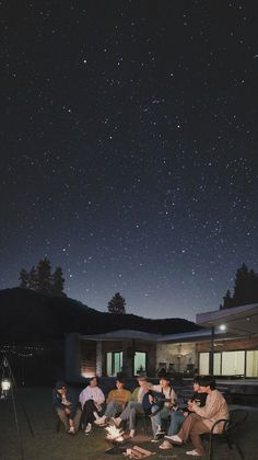 people sitting around a campfire at night with the stars in the sky above them