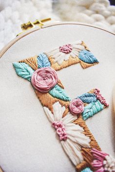 a cross stitched in to a white fabric with pink and blue flowers on it