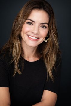 a smiling woman with her arms crossed, wearing black shirt and gold hoop earring