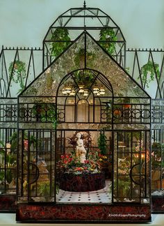 a glass house with plants and flowers in the front window, surrounded by wrought iron fencing