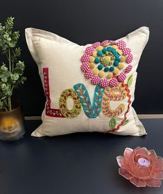 a decorative pillow sitting on top of a table next to a potted plant and candle