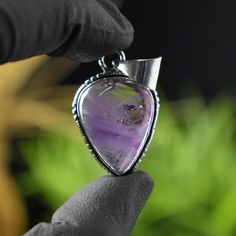 a person is holding a pendant with a purple stone in the shape of a triangle