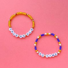 two beaded bracelets with words on them sitting next to each other against a pink background