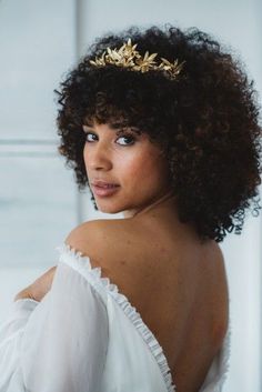 a woman with curly hair wearing a white dress and a gold tiara on her head