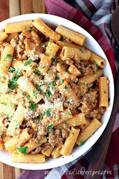 pasta with meat and parmesan cheese in a white bowl on a wooden table