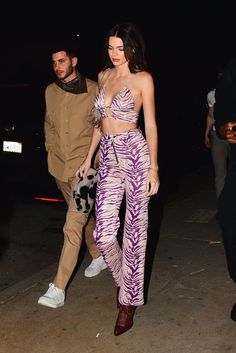 a woman in purple and white outfit walking next to a man