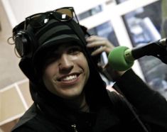 a man wearing headphones and a beanie smiles while holding a microphone in front of him