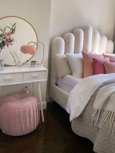 a white bed sitting next to a pink ottoman on top of a wooden floor