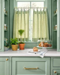 a kitchen with green cabinets and white counter tops, along with a window covered in sheer curtains