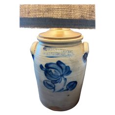 a blue and white urn with a lamp on it's side next to a burlap shade