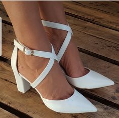 a woman's legs wearing white high heels with cross straps and a book on the floor