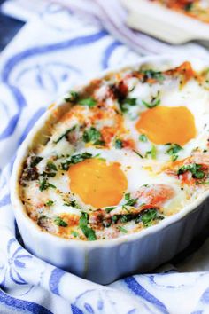 two eggs are in a white dish on a blue and white table cloth next to some bread