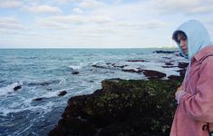 a woman standing on top of a rocky beach next to the ocean