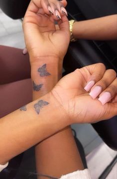 two women with matching tattoos on their arm and wrist, both holding each other's hands