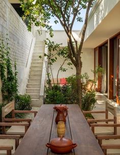 an outdoor dining area with wooden table and chairs, surrounded by plants and stairs that lead up to the second floor