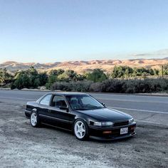 a black car parked on the side of a road in front of some hills and trees