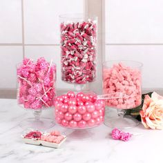 pink and white candies in glass vases next to flowers on marble counter top