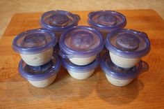 six baby food containers sitting on top of a wooden table next to a knife and fork