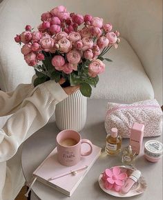 pink flowers in a white vase on a table with personal care items and makeup products