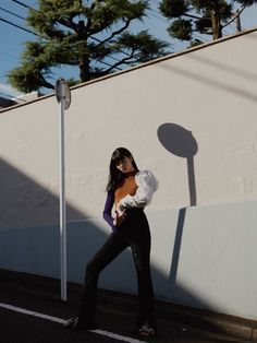 a woman is walking down the street with an orange bag in her hand and wearing black pants