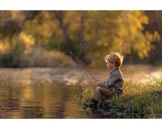 a little boy sitting on the bank of a river fishing