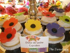 there are many cupcakes with flowers on the top and one has a sign that says dulce de leche cupcakes