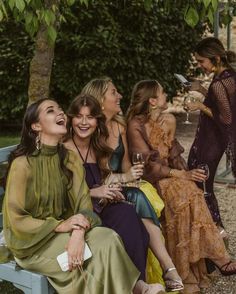 four women sitting on a bench laughing and drinking wine in front of some other people