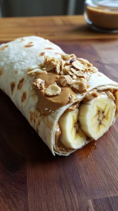 a tortilla wrap with peanut butter and banana slices on it sitting on a wooden table