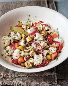 a white bowl filled with cauliflower, carrots and other vegetables on top of a table