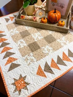 an orange and white quilted table runner with pumpkins in the basket on top