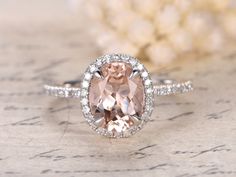 an oval shaped morganite and diamond ring on top of a piece of paper with flowers in the background