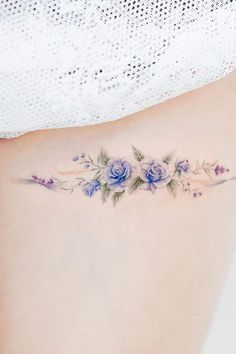 a woman's lower back tattoo with blue flowers and leaves on her side ribcage