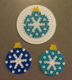 three ornaments made out of plastic beads on a table top, one is blue and the other is white