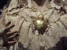 a close up of a person wearing a white dress and holding a heart shaped brooch