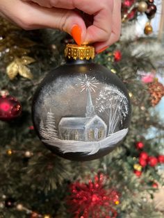 a hand holding an ornament with a church on it and fireworks in the sky