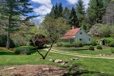 a house in the middle of a lush green field with rocks and trees around it